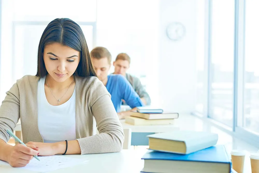 Estudiante tomando apuntes en un aula mientras prepara su tesis o proyecto académico.